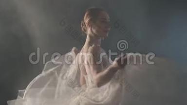 优雅的芭蕾舞演员穿着白色连衣裙，在黑暗中用灯光和烟雾舞蹈古典或现代芭蕾的元素